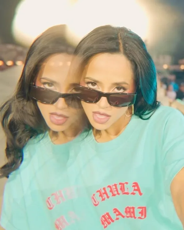 Η Becky G με γυαλιά ηλίου και τυρκουάζ μπλούζα με γράμματα, προμοτάρει το νέο της τραγούδι «Baraja Bendita».