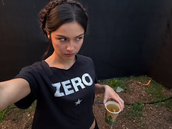 Η Olivia Rodrigo με μαύρο t-shirt και αναφορά στο «The Handmaid’s Tale» κρατάει ένα ποτήρι.