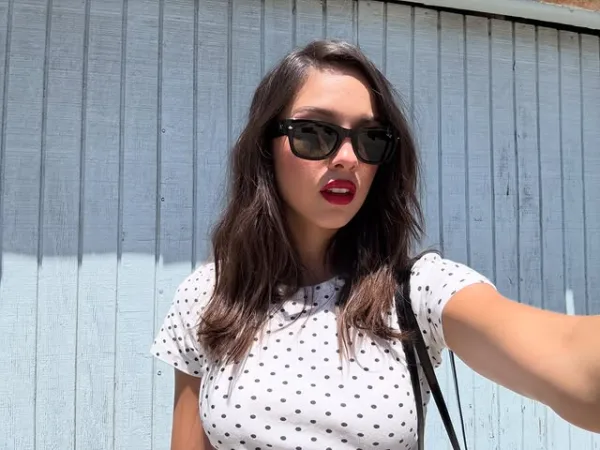 Η Olivia Rodrigo με γυαλιά ηλίου και πουά μπλούζα γιορτάζει τα 400 εκατομμύρια streams του τραγουδιού της στο Spotify.
