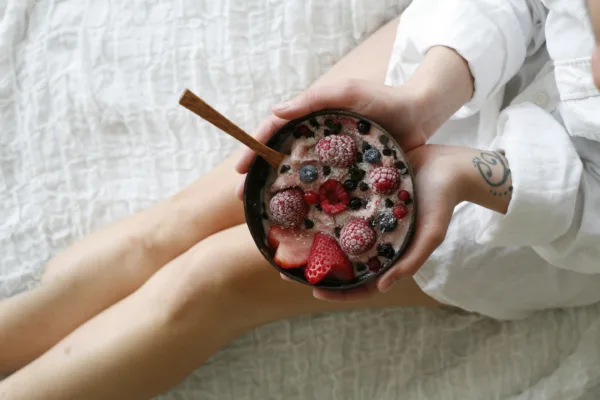 Γυναίκα κρατά μπολ με smoothie, βρώμη και φρέσκα φρούτα