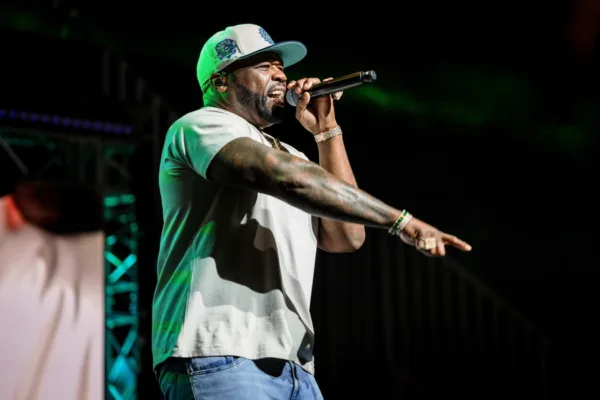 Ο 50 Cent τραγουδάει με μικρόφωνο, φορώντας καπέλο και κοσμήματα, στο πλαίσιο της προώθησης του νέου «Street Fighter».
