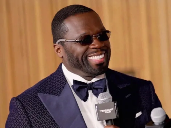 Ο 50 Cent χαμογελάει φορώντας γυαλιά ηλίου και κοστούμι, ενώ κρατάει μικρόφωνο στο NFL.