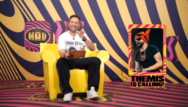 Ο Akylas μιλάει για την Eurovision στο «OK! Themis» με φόντο το λογότυπο MAD και μια εικόνα του ίδιου.