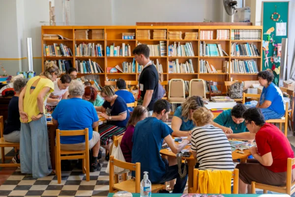 Συμμετέχοντες σε εργαστήριο κατά τη διάρκεια του Φεστιβάλ ANIMASYROS, με ράφια γεμάτα βιβλία στο φόντο.