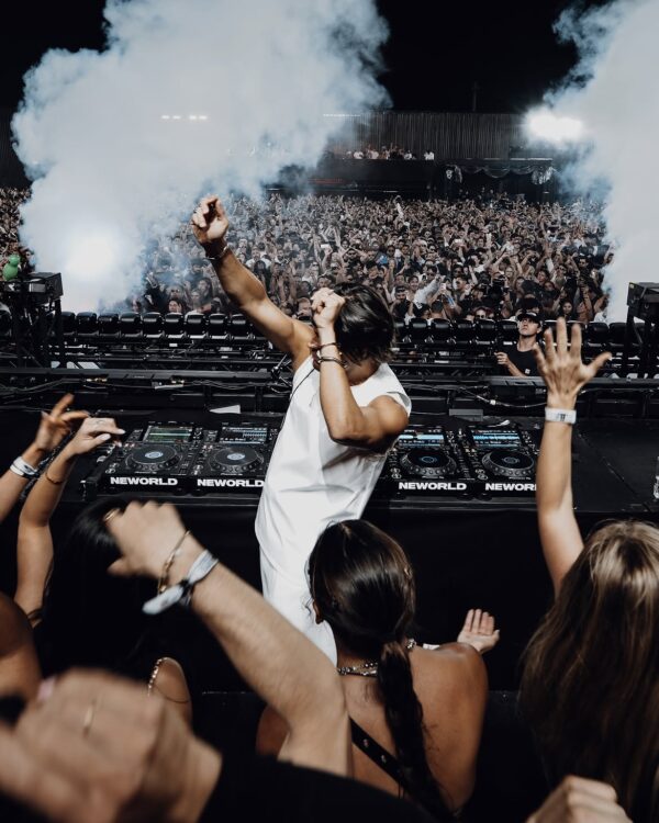 Ένας DJ παίζει μουσική μπροστά σε ένα μεγάλο πλήθος, ενώ καπνός ανεβαίνει στον αέρα κατά τη διάρκεια της συναυλίας.
