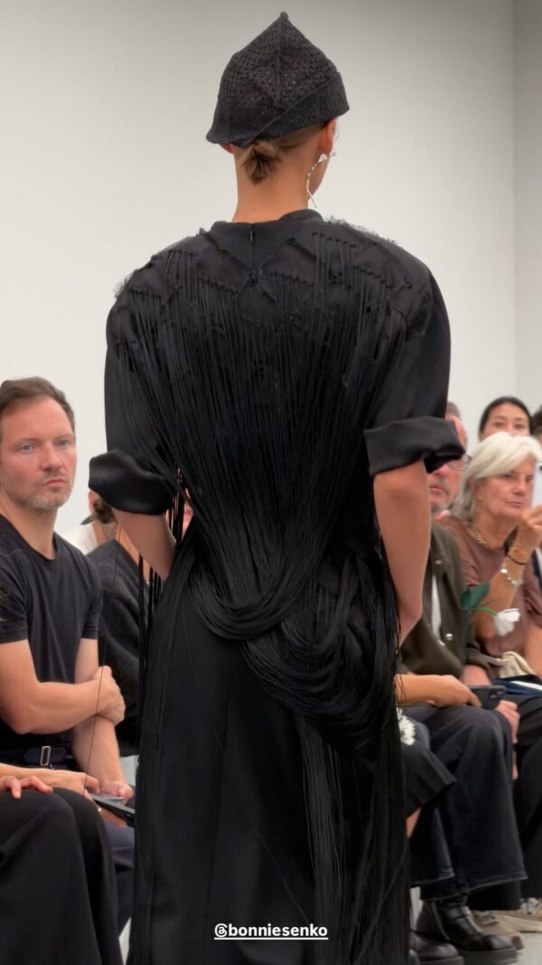 Μοντέλο παρουσιάζει τη νέα συλλογή Bottega Veneta SS27 με ένα εντυπωσιακό μαύρο φόρεμα με κρόσσια και καπέλο.