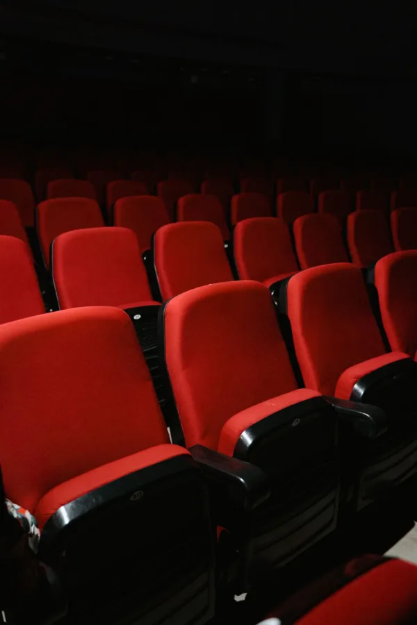 Άδειες κόκκινες καρέκλες σε σκοτεινή αίθουσα κινηματογράφου, περιμένοντας το κοινό για την πρεμιέρα της νέας ταινίας.