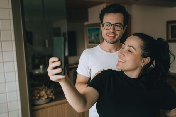 Ζευγάρι τραβάει selfie με κινητό, εξερευνώντας το δίλημμα του soft ή hard launching στα social media.