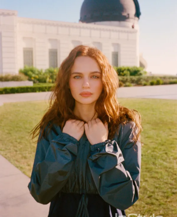 Η Joey King ποζάρει με κόκκινα μαλλιά και μπλε μάτια, με φόντο ένα κτίριο και πάρκο.