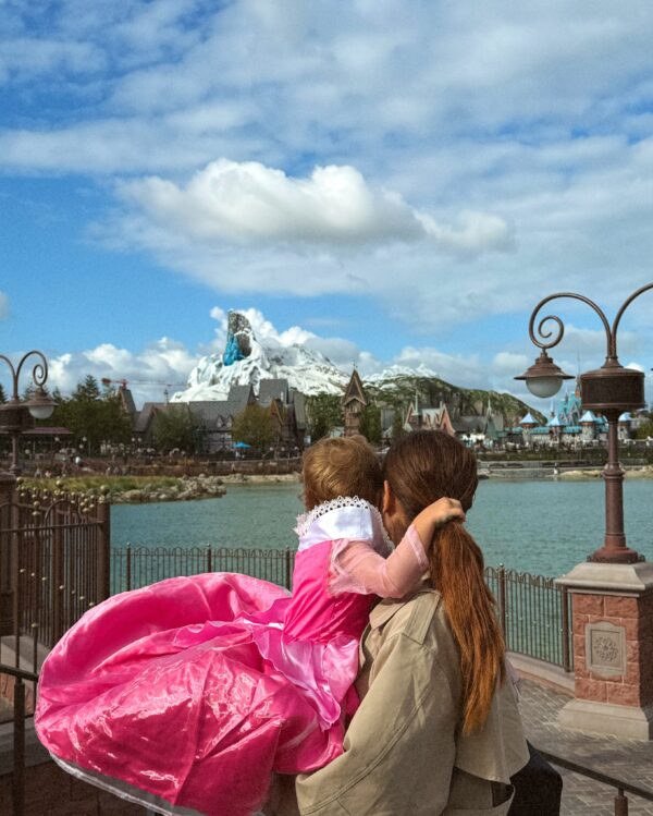 Η Μαίρη Συνατσάκη κρατάει την κόρη της στην Disneyland, με φόντο το μαγευτικό τοπίο του πάρκου.
