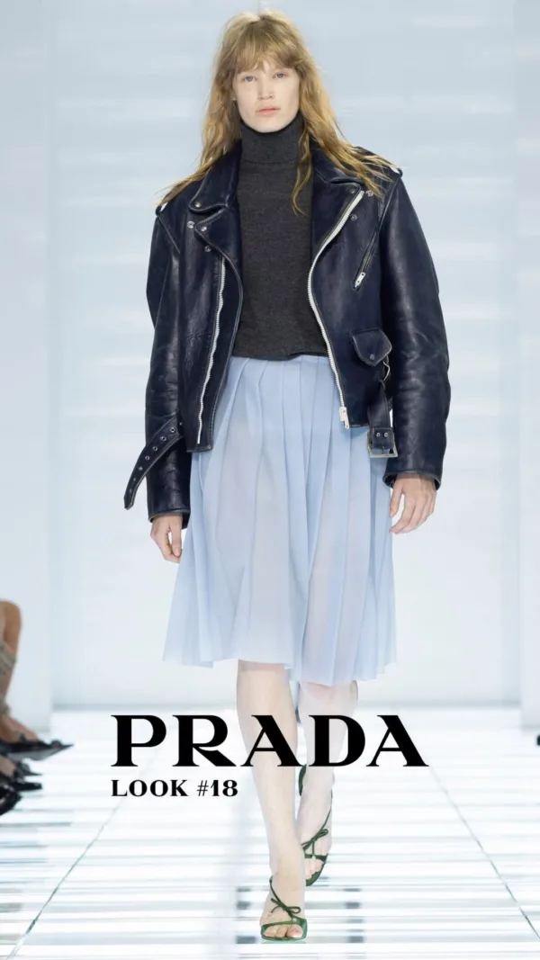 Μοντέλο παρουσιάζει δημιουργία του οίκου Prada με δερμάτινο τζάκετ και αέρινη φούστα, επαναπροσδιορίζοντας τη θηλυκότητα.