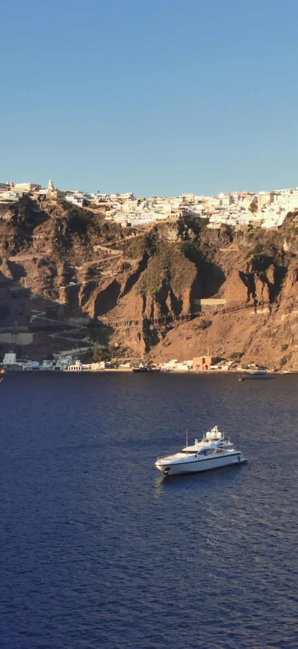 Η Σαντορίνη με το χαρακτηριστικό τοπίο και ένα πολυτελές γιοτ να πλέει στα γαλάζια νερά του Αιγαίου.