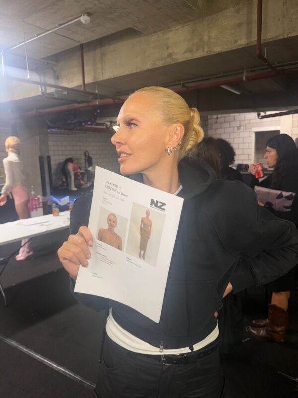 Η Τάμτα στο London Fashion Week κρατάει χαρτιά με φωτογραφίες της, ετοιμάζοντας την εμφάνισή της.