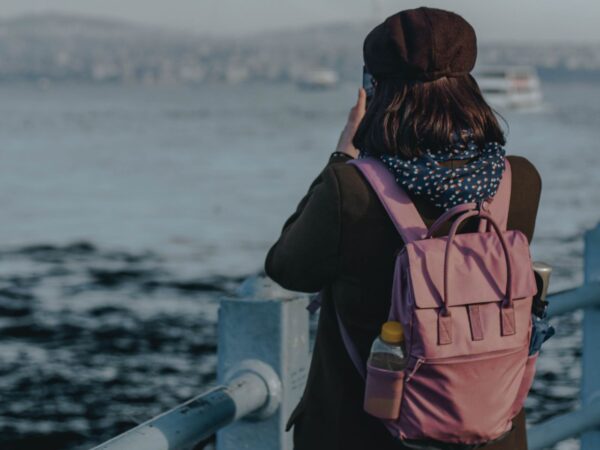 Γυναίκα με μωβ σακίδιο πλάτης φωτογραφίζει τη θάλασσα, απολαμβάνοντας την απόδραση και αλλάζοντας τη διάθεσή της.