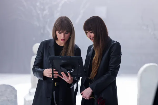 Δύο γυναίκες κοιτούν ένα tablet σε ένα σκοτεινό σκηνικό, με αμυδρά μνημεία στο φόντο, για το νέο music video.