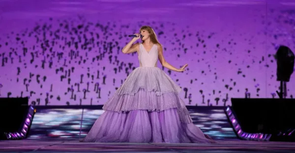Η Taylor Swift τραγουδάει με εντυπωσιακή μωβ τουαλέτα σε σκηνή με φόντο αμερικανικό ποδόσφαιρο.