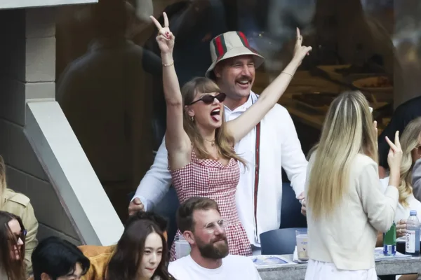 Η Taylor Swift και ο Travis Kelce γιορτάζουν σε αγώνα, με την Taylor να δείχνει δύο δάχτυλα σε σχήμα V.