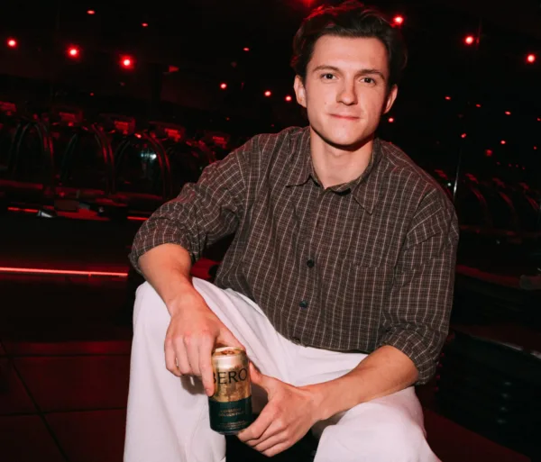 Ο Tom Holland, ο πιο εμπορικός ηθοποιός όλων των εποχών, κρατάει ένα κουτάκι μπύρας σε εσωτερικό χώρο με κόκκινο φωτισμό.