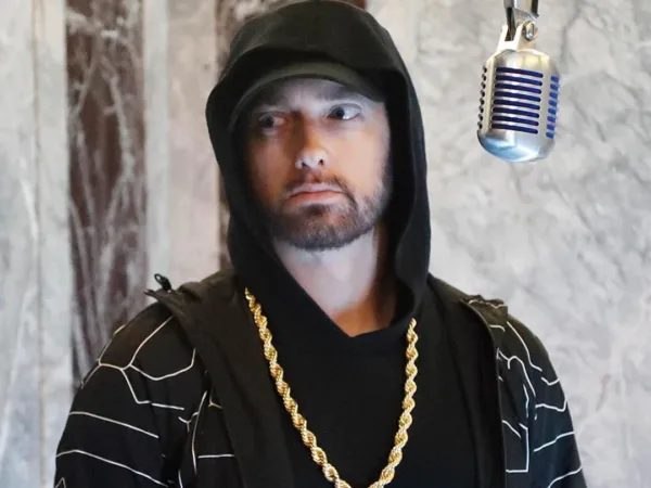 Ο Eminem ποζάρει με χρυσή αλυσίδα και κουκούλα δίπλα σε ένα μικρόφωνο, σε σκηνή σχετική με διαρροή μουσικής.