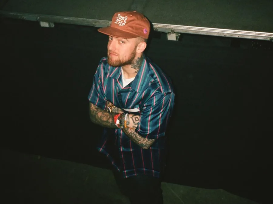 Ο Mac Miller με καπέλο και σταυρωμένα χέρια, σε σκηνή που σχετίζεται με την επανέκδοση του άλμπουμ «The Divine Feminine».