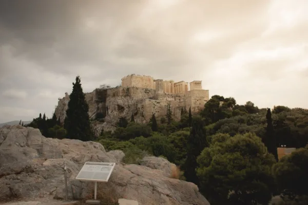 Η Ακρόπολη της Αθήνας δεσπόζει επιβλητικά με τα αρχαία μνημεία της, περιτριγυρισμένη από πράσινο και με συννεφιασμένο ουρανό.