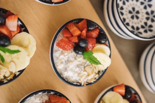 Μια σειρά από μπολ με overnight oats, γαρνιρισμένα με φρέσκες φράουλες, μύρτιλα, μπανάνα και αμύγδαλα, παρουσιάζουν ένα υγιεινό πρωινό.