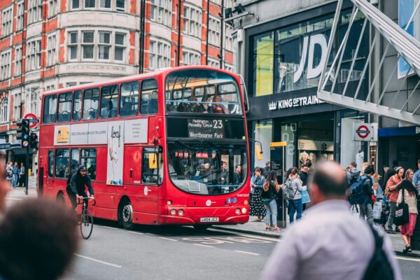 Κόκκινο διώροφο λεωφορείο κινείται στην Oxford Street, με πεζούς και καταστήματα να διακρίνονται στο φόντο, για τα Χριστούγεννα στο Λονδίνο.