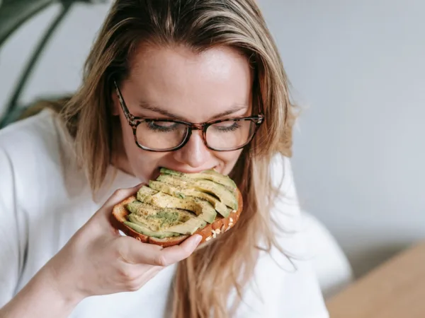Γυναίκα τρώει τοστ με αβοκάντο, ένα από τα superfoods που βοηθούν στη συγκέντρωση στο γραφείο.